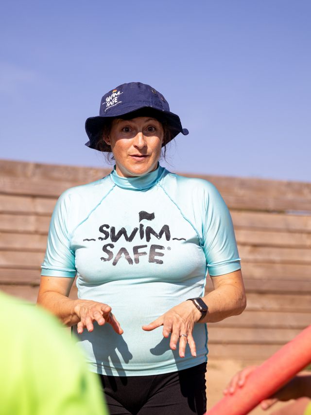 A person wearing a navy blue bucket hat and a light blue striped T-shirt with “Swim Safe” 